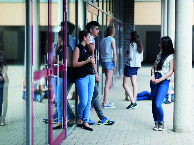Jugendliche stehen lässig vor der Schule. Es ist Pause.