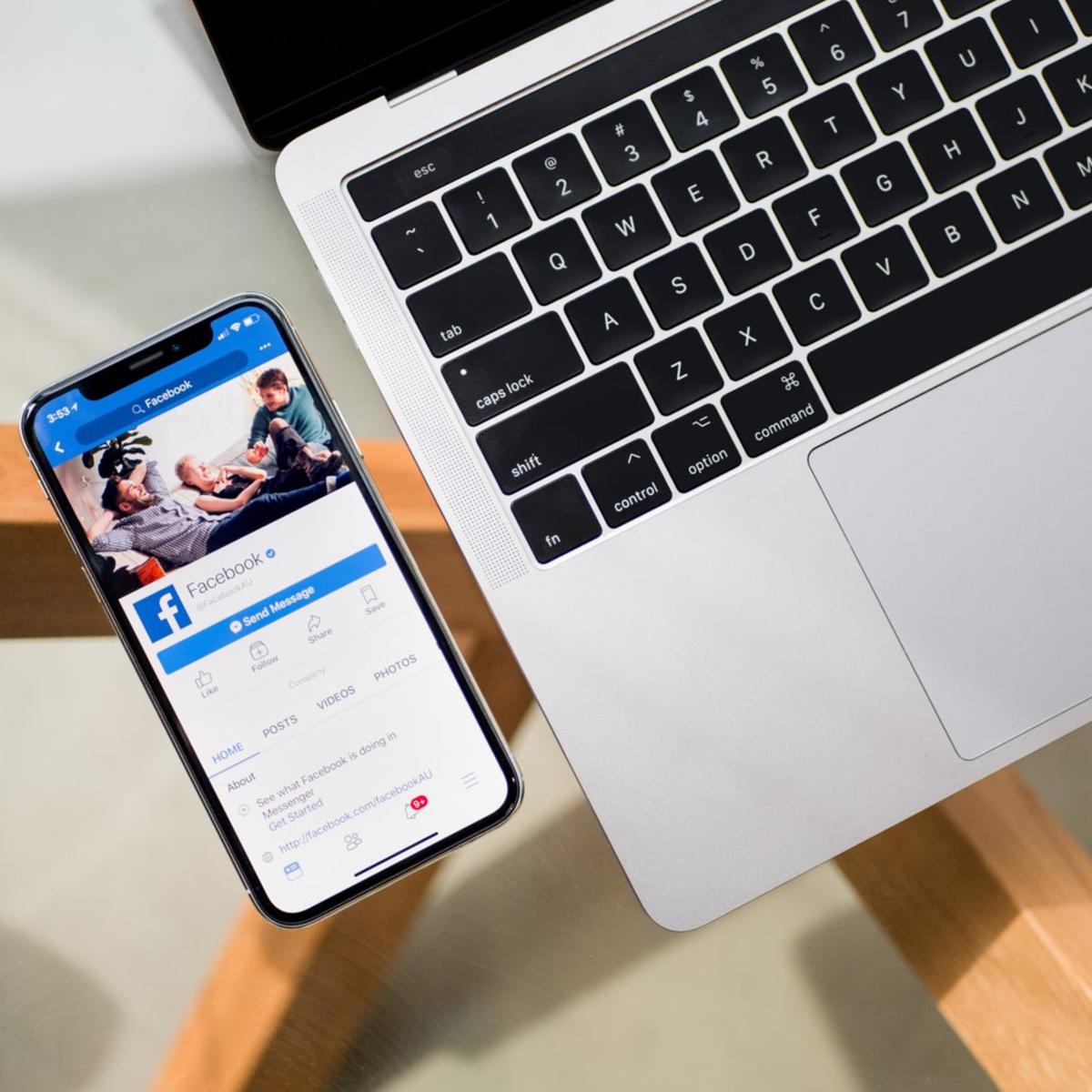 Laptoptastatur und daneben liegt ein Smartphone auf welchem Facebook zu sehen ist.