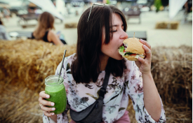 eine Frau beisst genüsslich in einen planted Burger und hat einen grünen Smoothie in der Hand